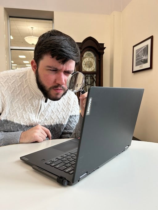 Person looking through magnifying glass at a laptop.