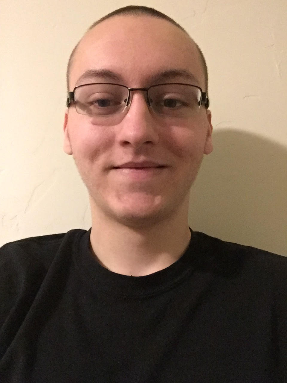 A young student with glasses standing in front of a wall.