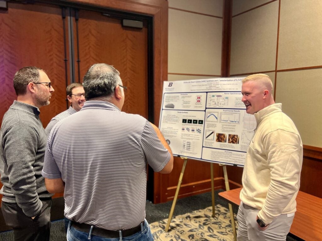 A student speaks to others on his research poster. 