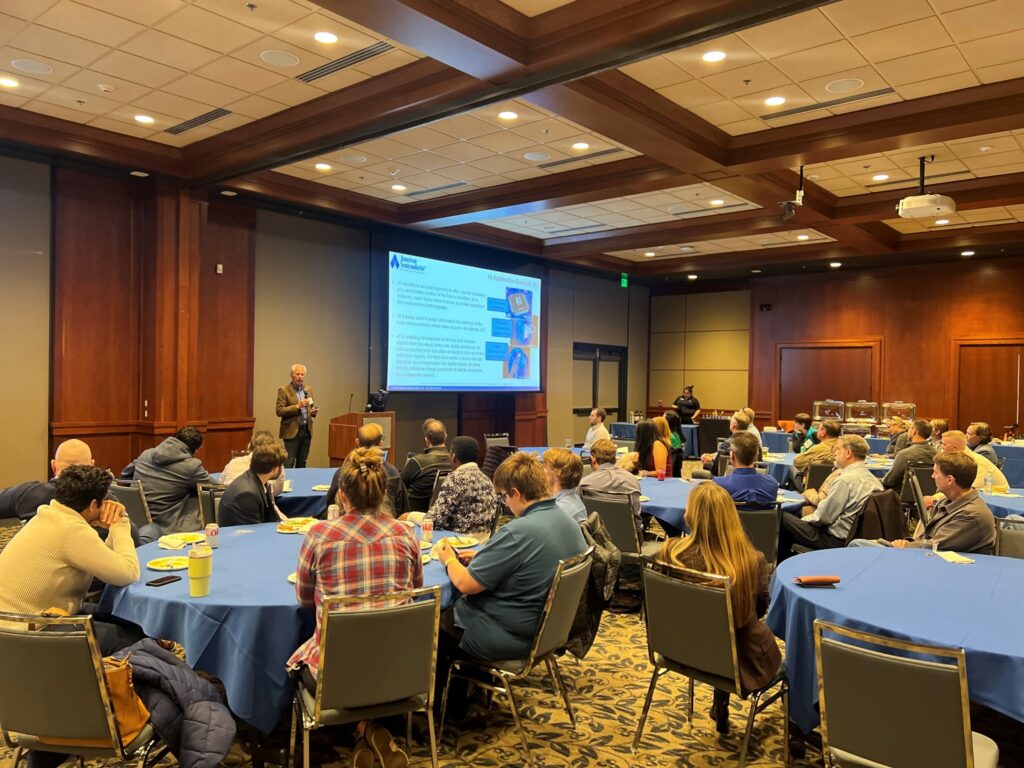 A presenter presenting in front a full crowd. 