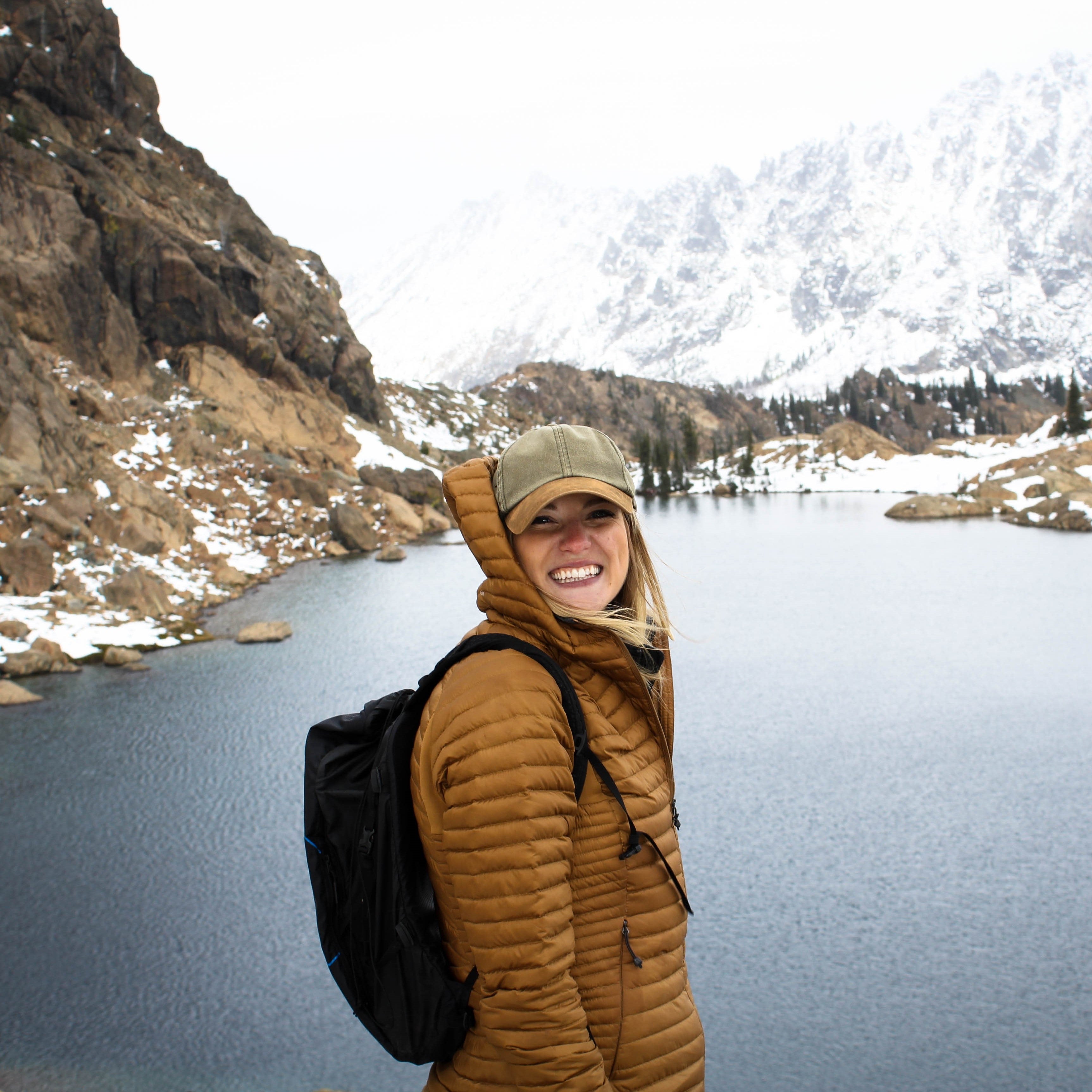 Smiling young woman with backpack in front of a river and mountains