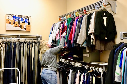 A young woman, with her back to the viewer, looks through racks of colorful blouses mounted on the opposite wall.
