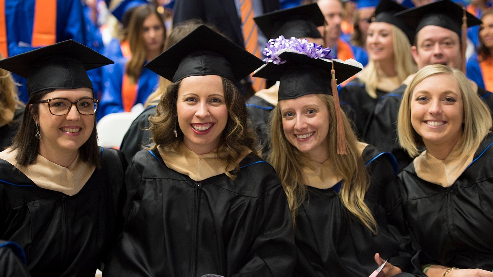 Four graduate students sit at commencement