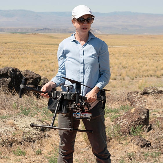 professor stands in drylands holding drone