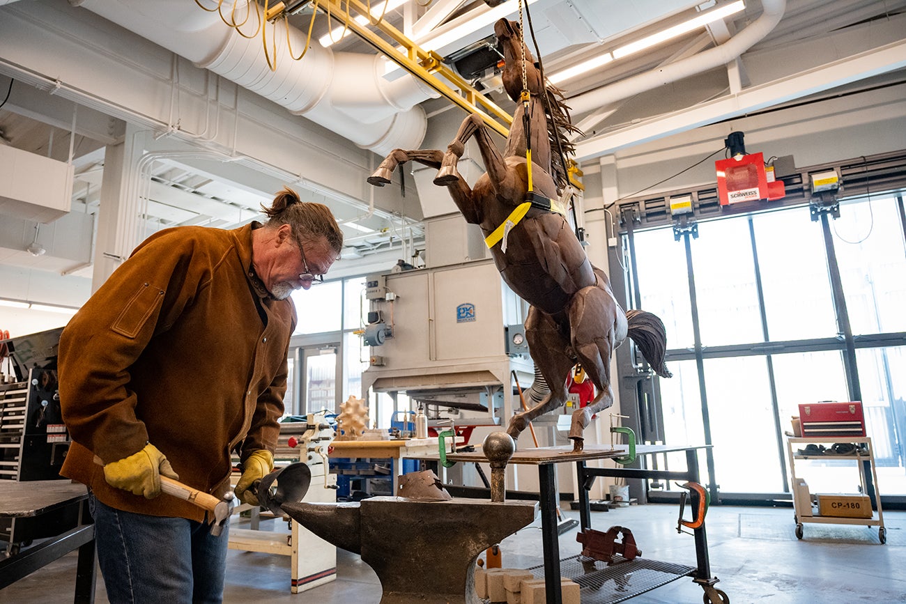 Fox is refashioning a steel hoof, with the Bronco sculpture hanging behind him from a harness