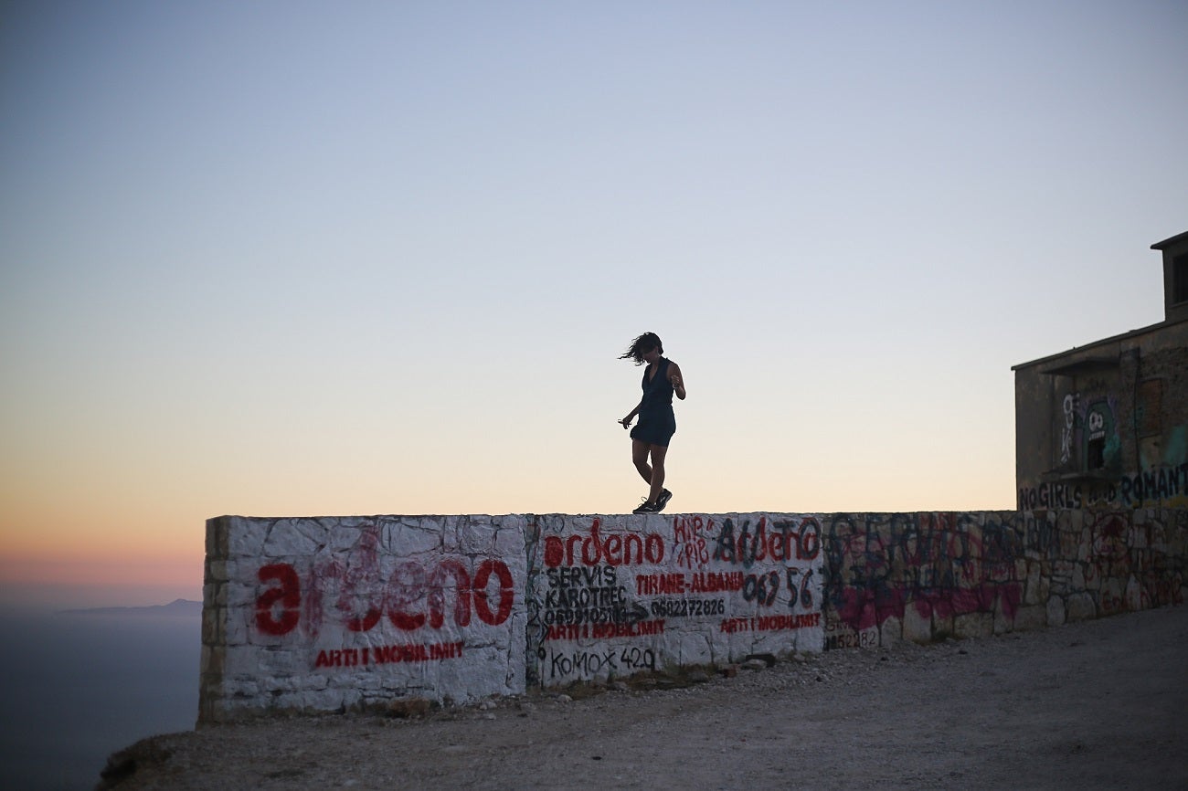 A female silhouetted against the sunset walking along a graffitied wall.