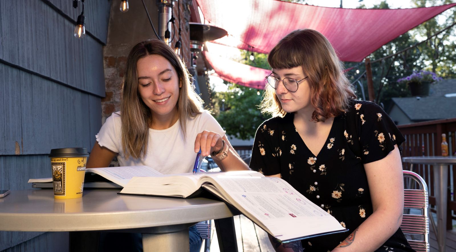 Two students sitting outside and looking at a textbook