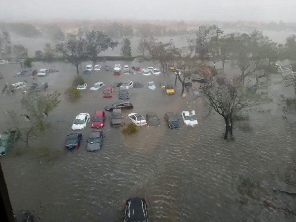 Floodwaters fill a parking lot during a storm, nearly covering the cars.