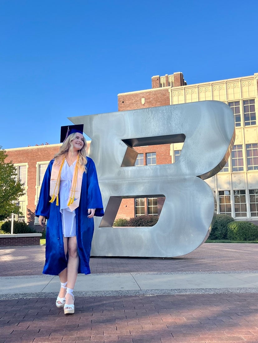 Amanda Pace wears her baccalaureate regalia in front of the silver Boise State B.