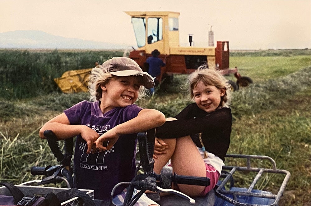 two little girls sit on four-wheeler in rural setting