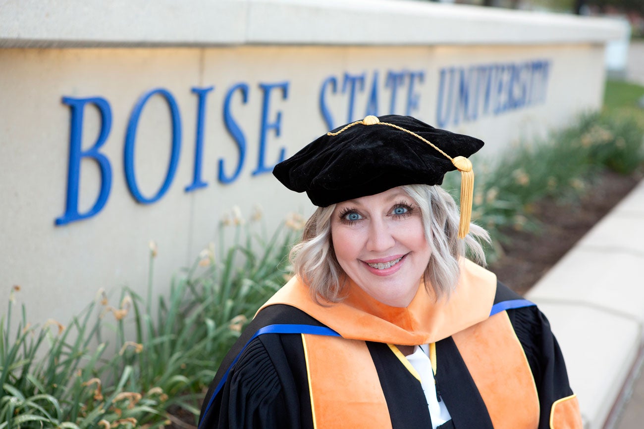 Debbie Ketchum wears her doctoral regalia in front of the Boise State University sign.