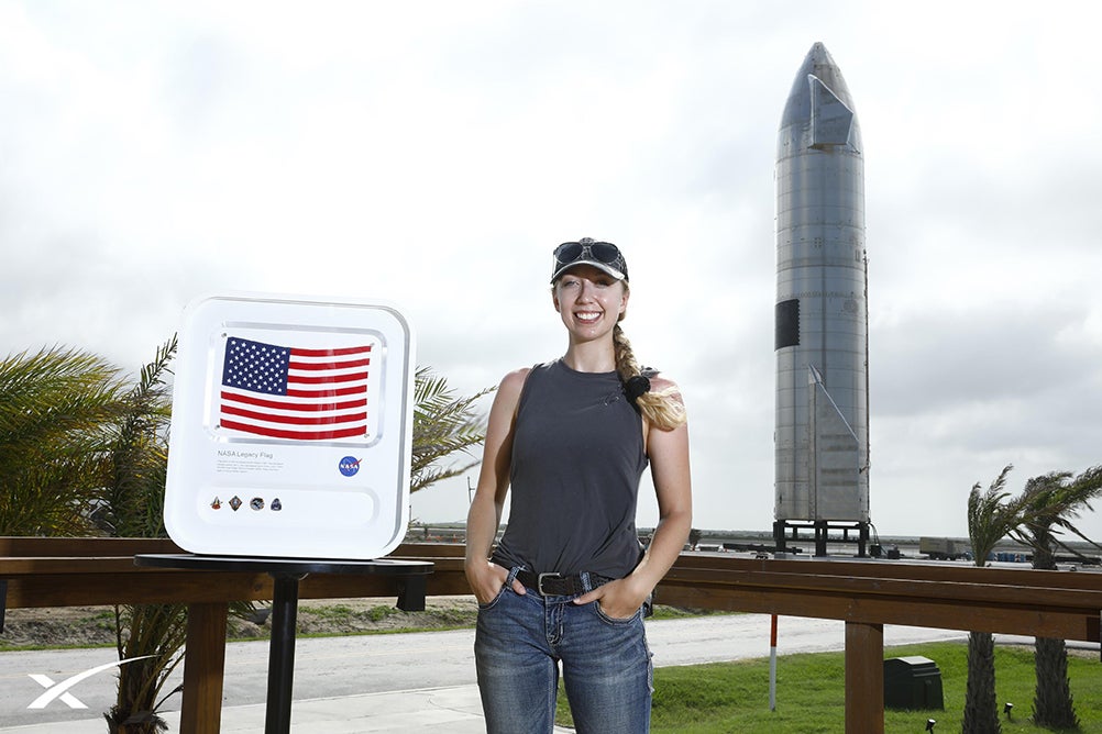 woman stands outside next to rocket artifact