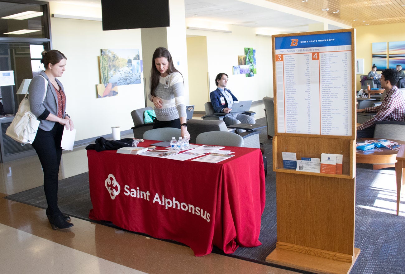 A hiring representative stands behind table in School of Nursing pointing out materials to a student