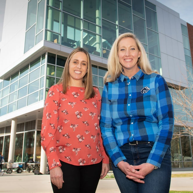 Aida Midgett and Katy Weiser stand side by side in front of Interactive learning building