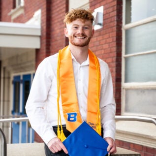 Zack Tyree, wearing his commencement regalia, poses on campus.