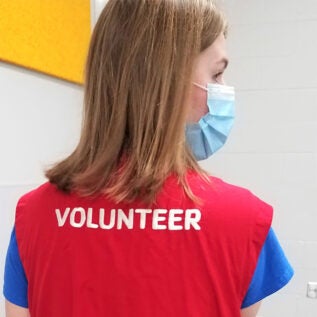 Rear view of an individual with blond hair wearing an orange vest that displays the word Volunteer.
