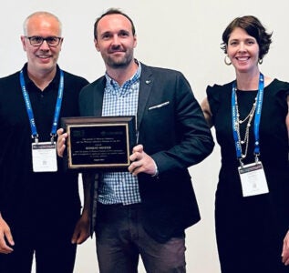 two men and one woman stand for posed photo, man in center hold award plaque