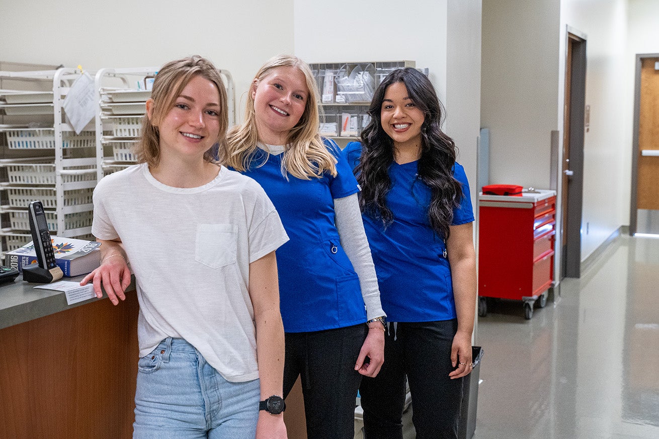 Three nursing students stand by the nurses' station in the Simulation Center.