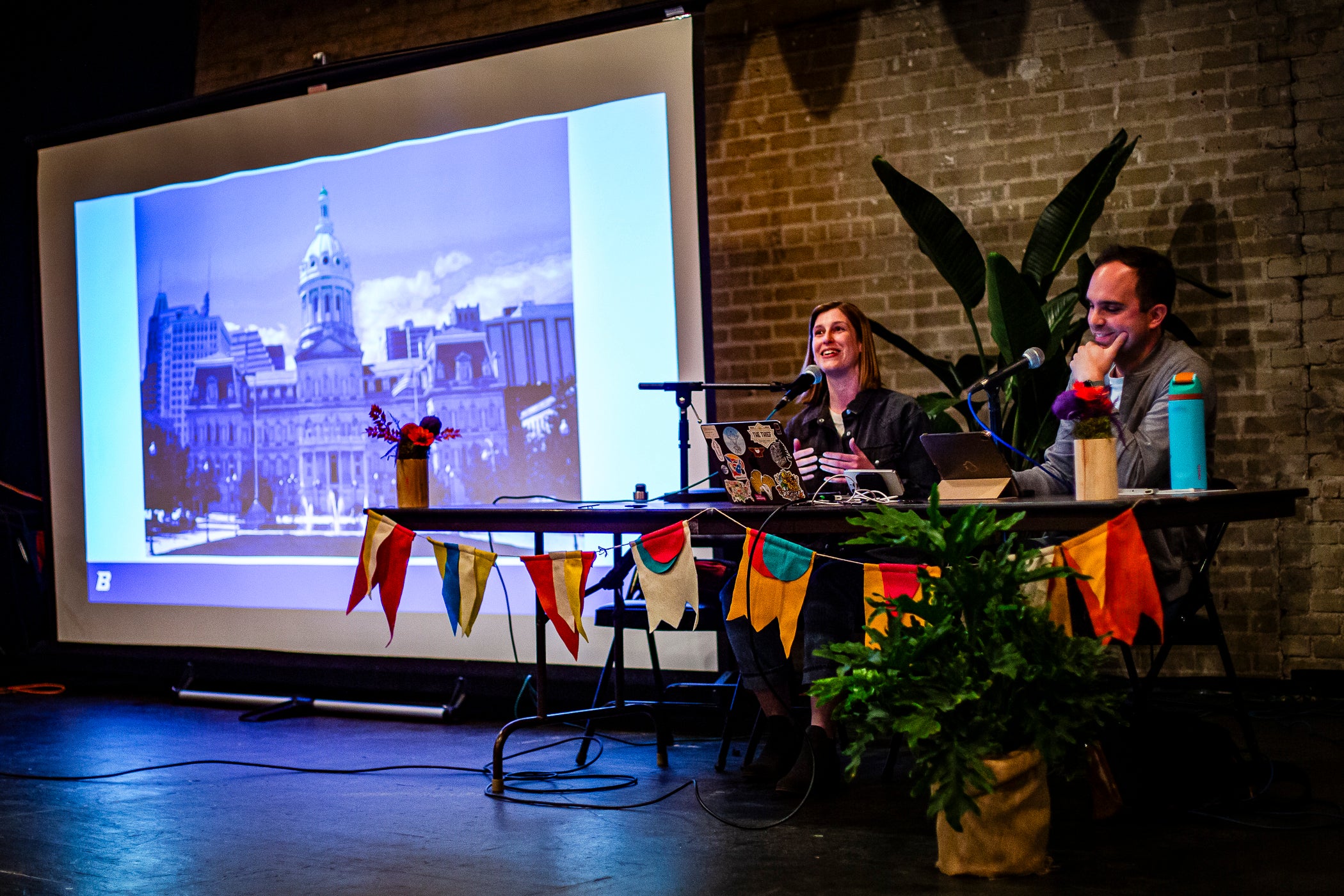 Two persons sit at a desk with microphones