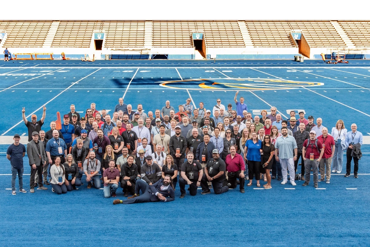 A large group of persons pose on the Albertsons Stadium field