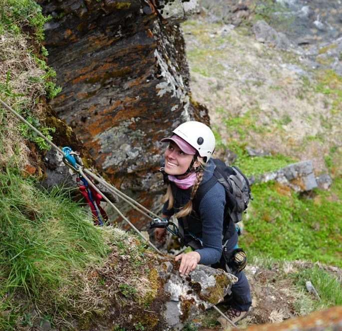 A person scales a rock face with climbing gear