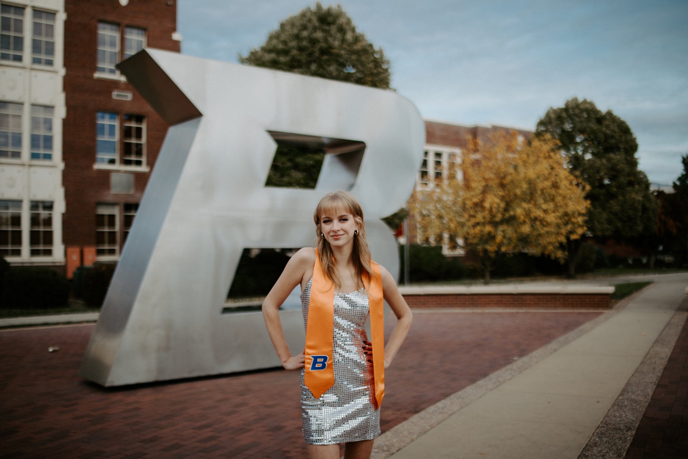 Sarah Carson poses in her graduation stole and a sparkly dress in front of the Boise State B