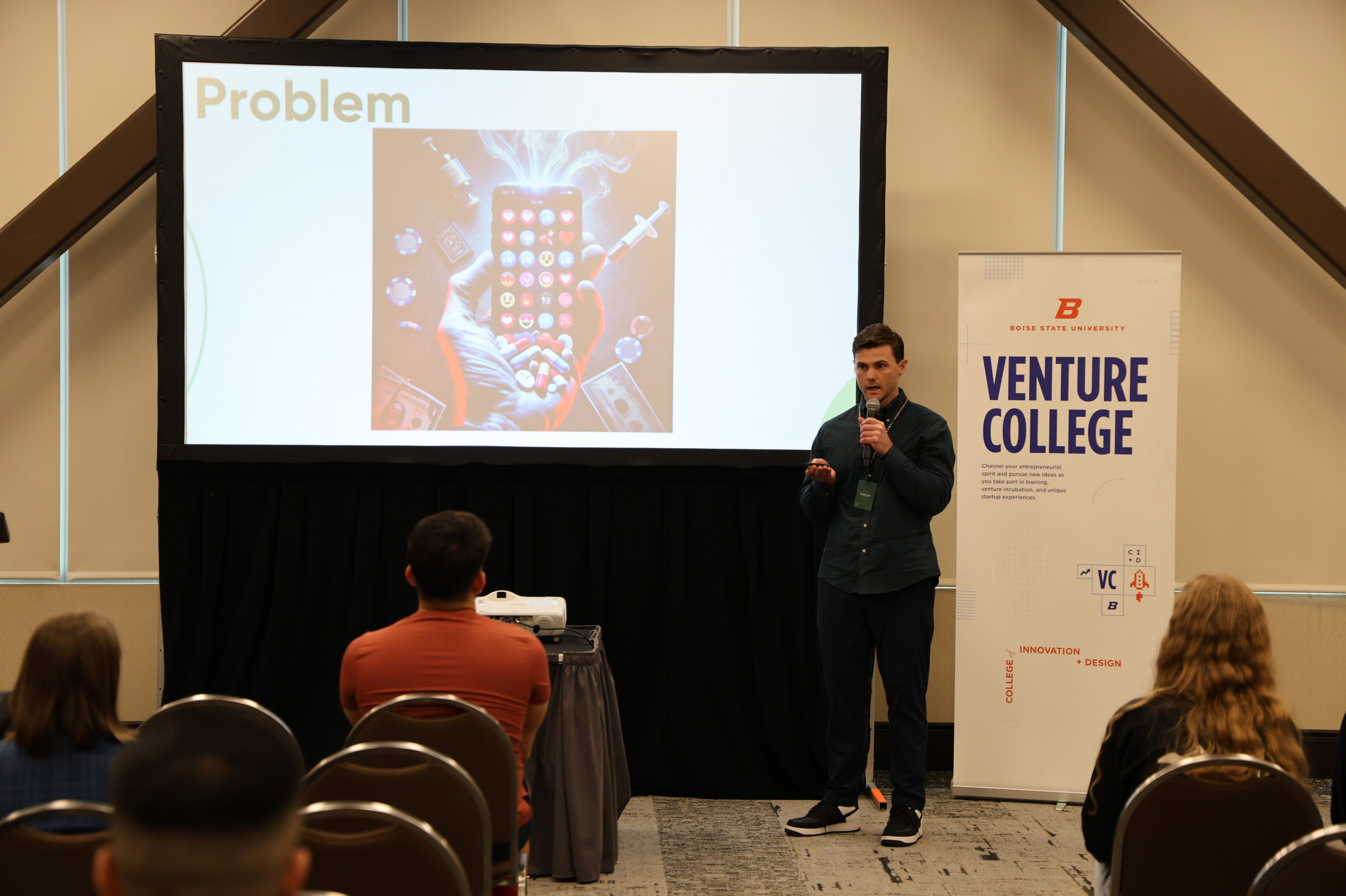 Luke Larkin stands before a slideshow. The slide reads "Problem" and includes a picture of a phone, pills and money.