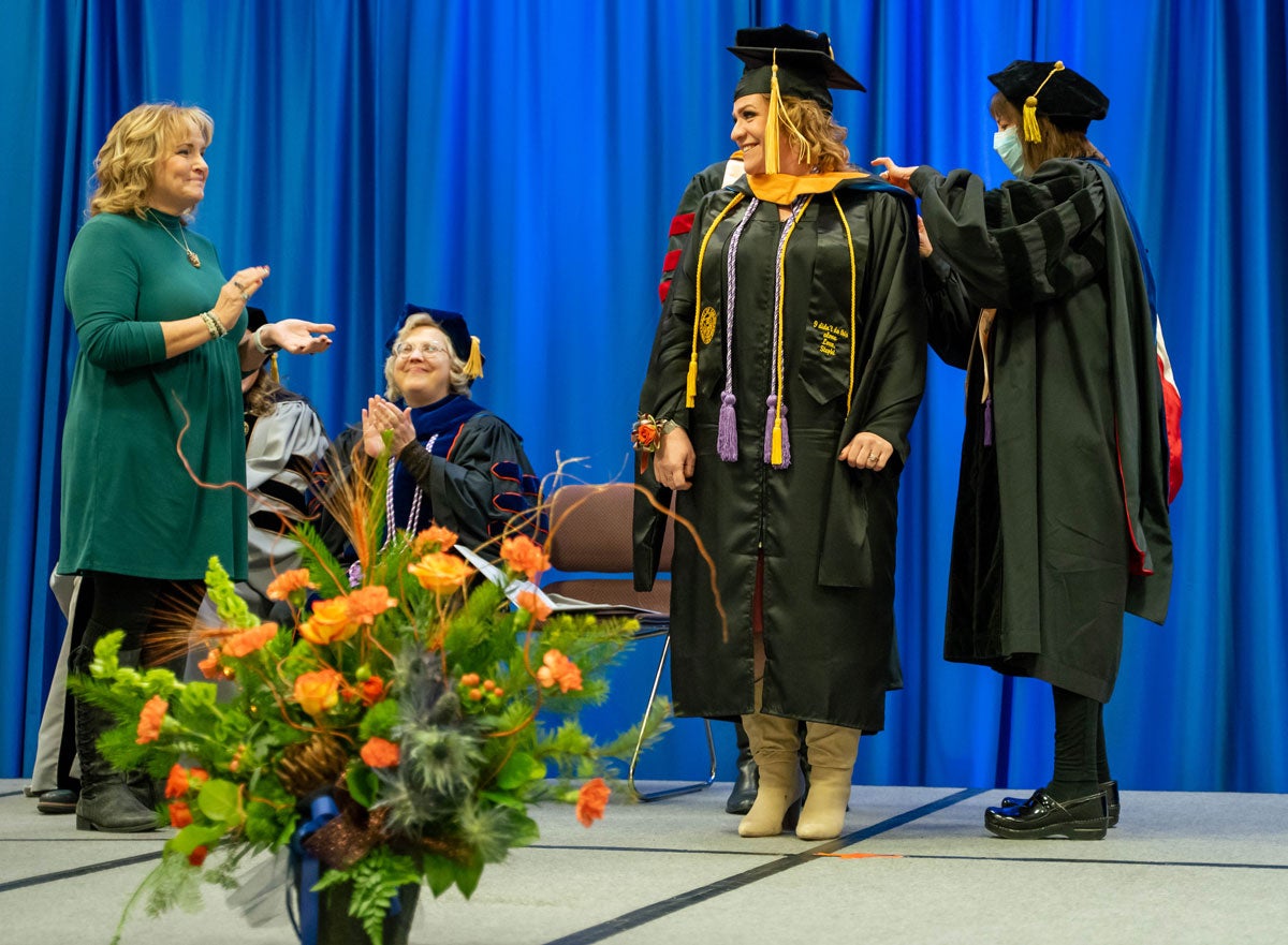 Stephanie Shawver stands on stage as AGNP professors arrange her hood.