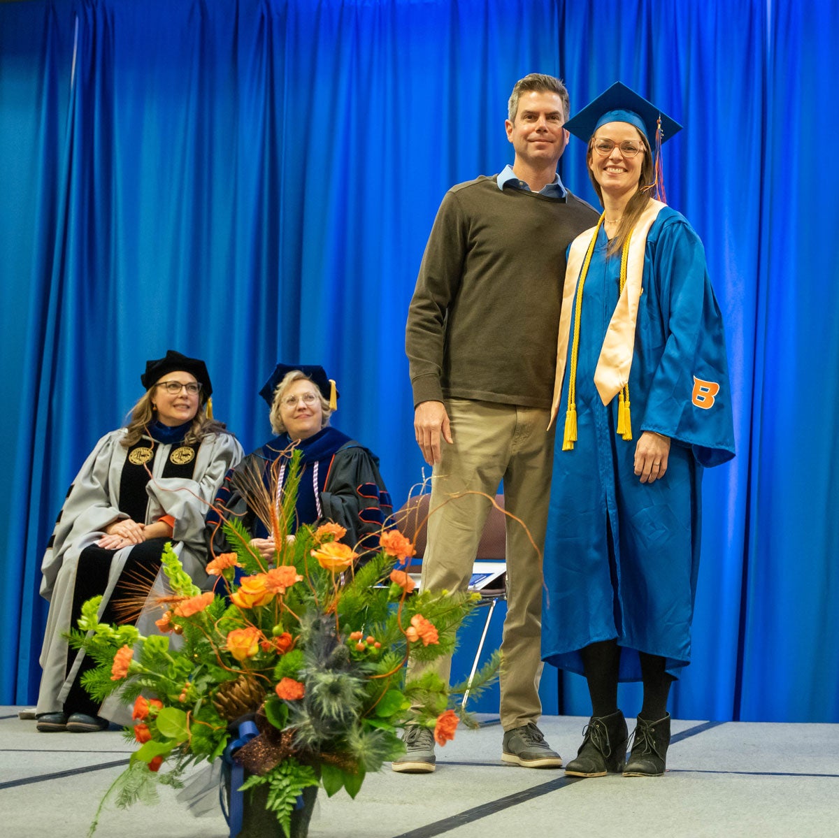 Quatraro and her husband stand on stage during Convocation. School of Nursing Deans sit in the background.