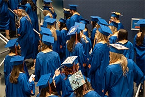 A large group of students in blue regalia ascend a staircase.