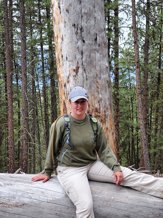 Brieann Jones sits on a bench in front of a large tree.