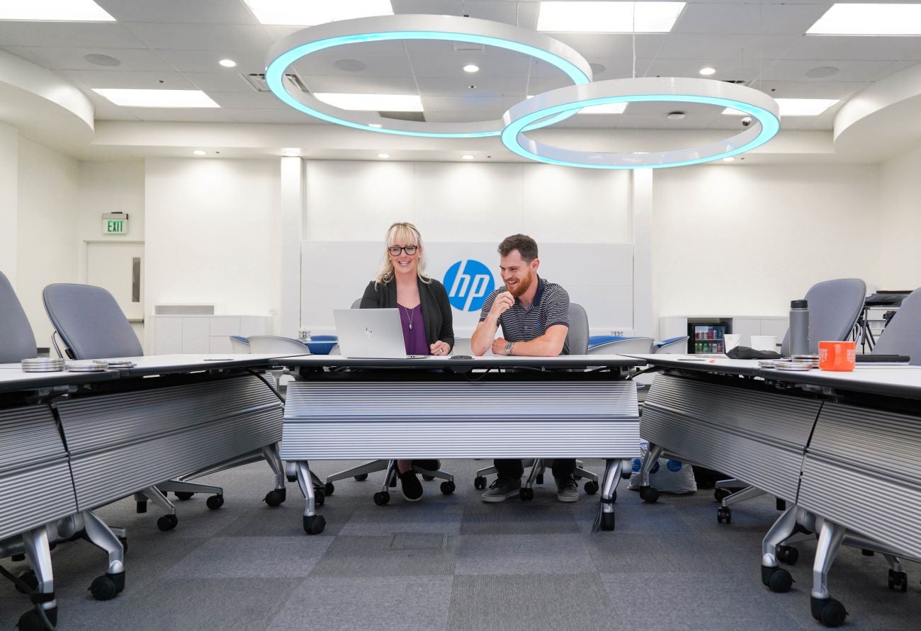 Kris Pruett and Adam Eschbach working on a laptop in front of a Hewlett-Packard logo