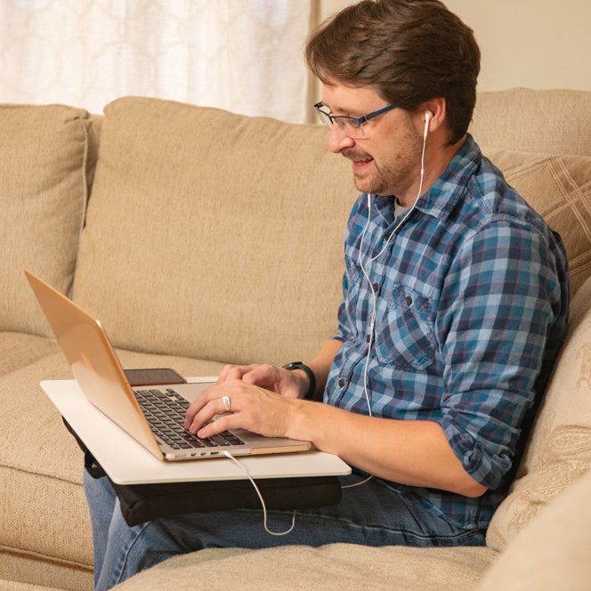 A male student sits on a couch with a laptop computer