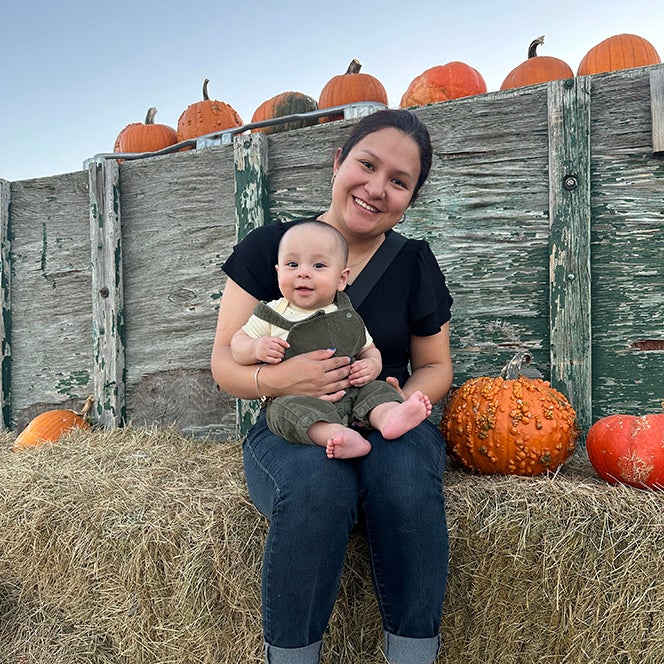 Jazmin Gallardo Carrillo sitting on a bale of hay with her child