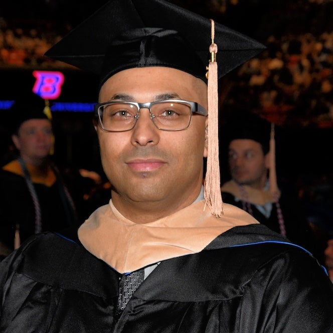 James Young, a recent Boise State graduate, is wearing a cap and gown while attending a commencement ceremony.