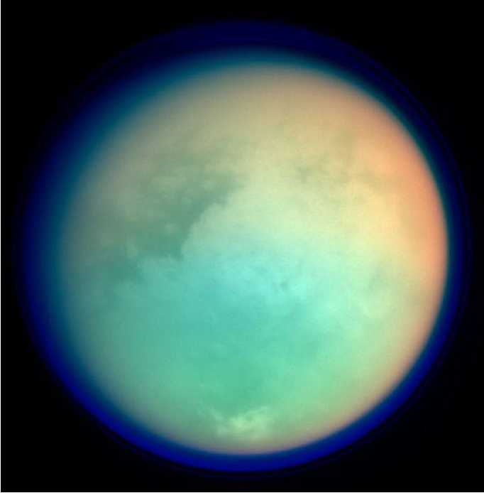 Saturn's moon Titan seen in false color, showcasing its hazy, dense atmosphere with vivid gradients.