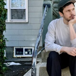 Tom rests his hand on his chin while looking slightly to the right on the stoop of an old building.
