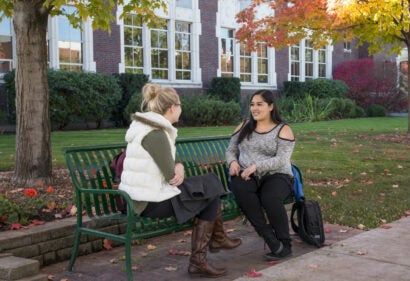 Megan Forristall and Estefany Vega sitting on a bench in front of admin building