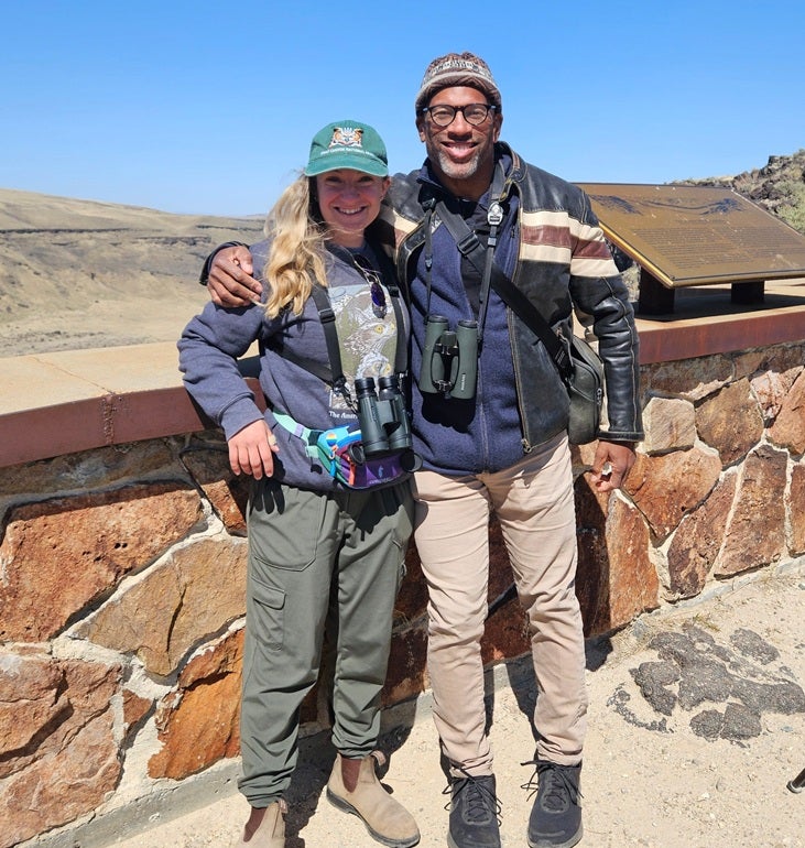Photo of Zoe Bonerbo and Christian Cooper Zoe Bonerbo and Christian Cooper in the field with binoculars and field clothing, smiling