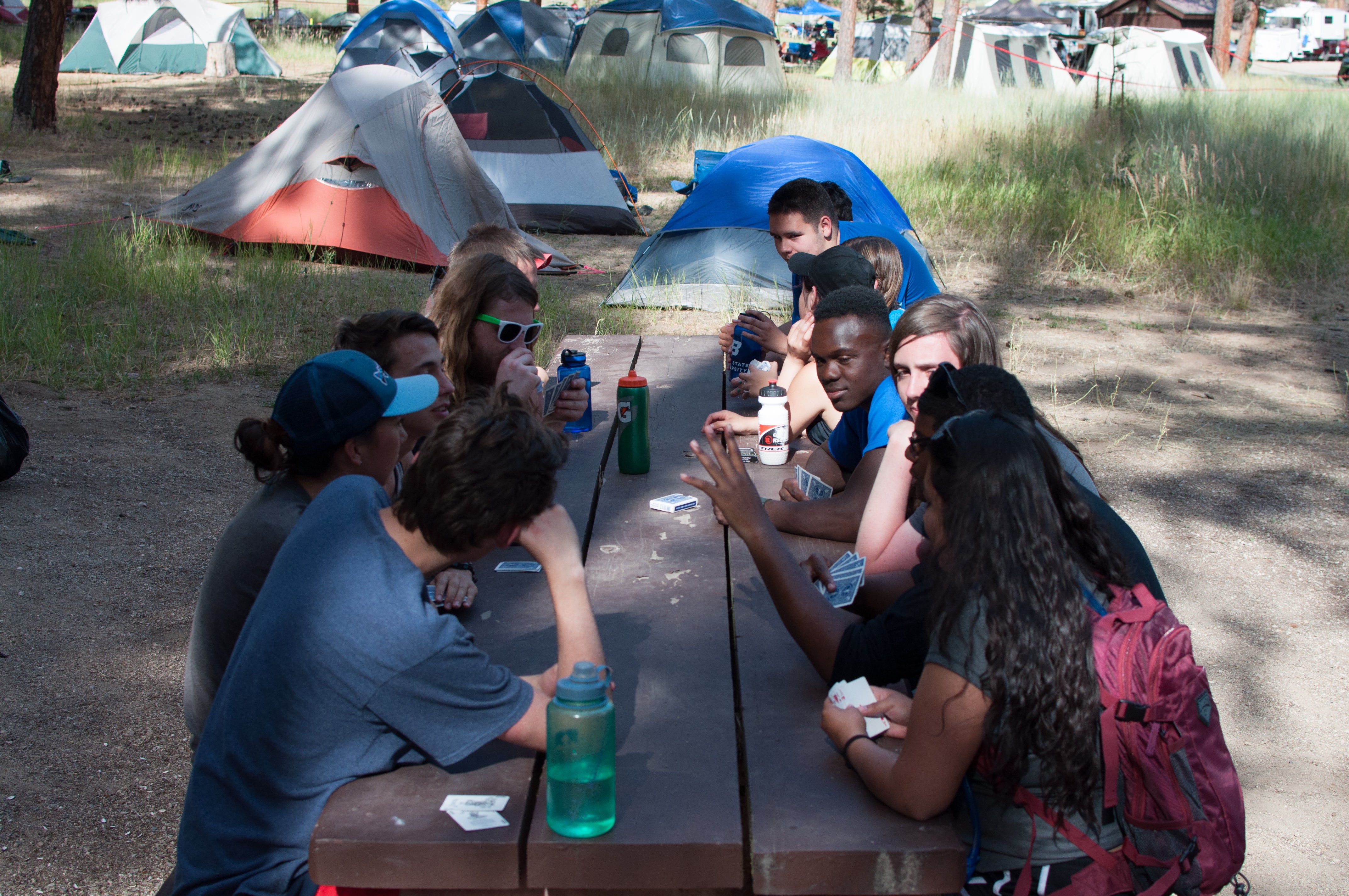 Campers playing cards around a picnic table.