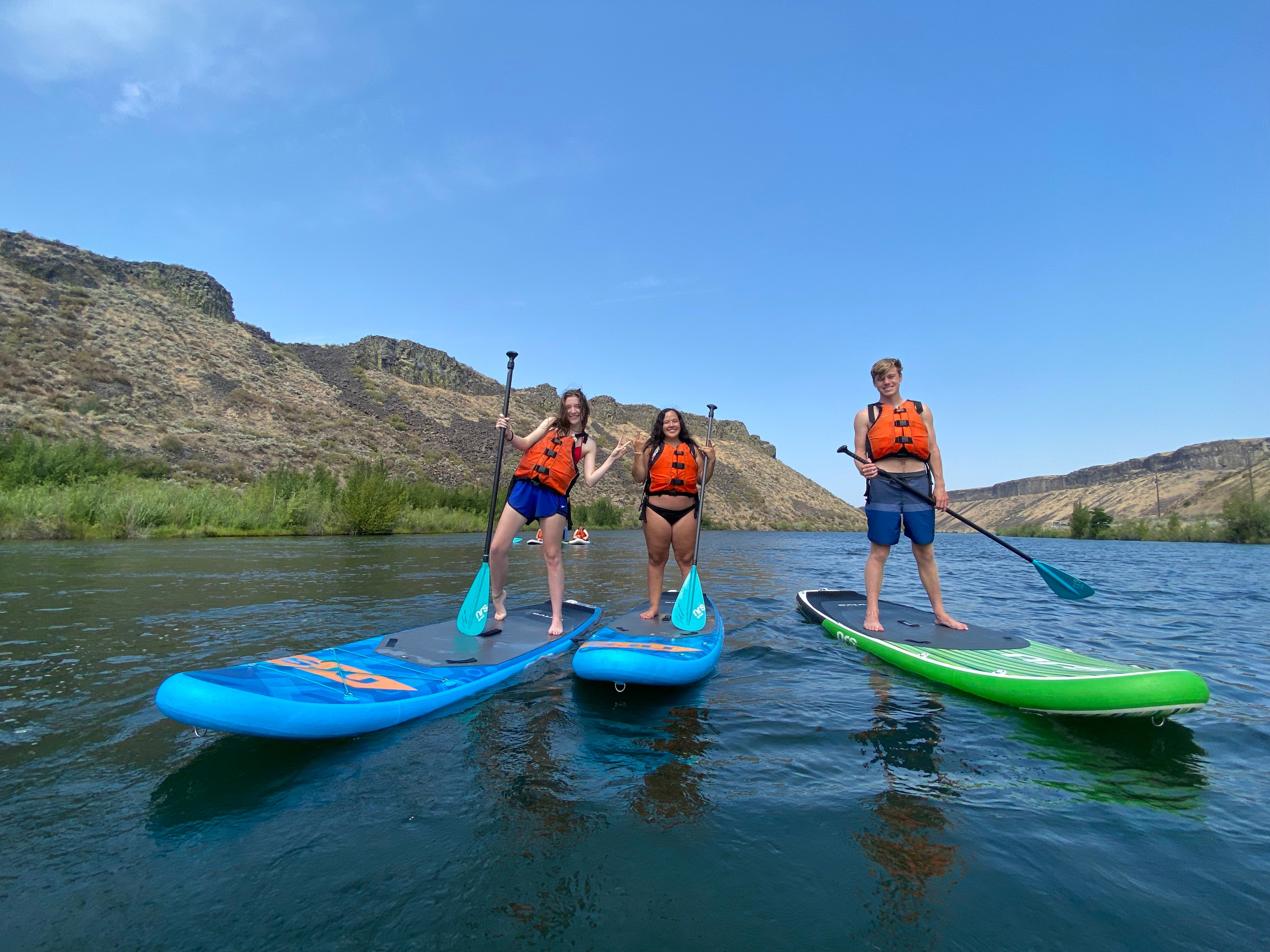 Students stand on paddle boards on the river