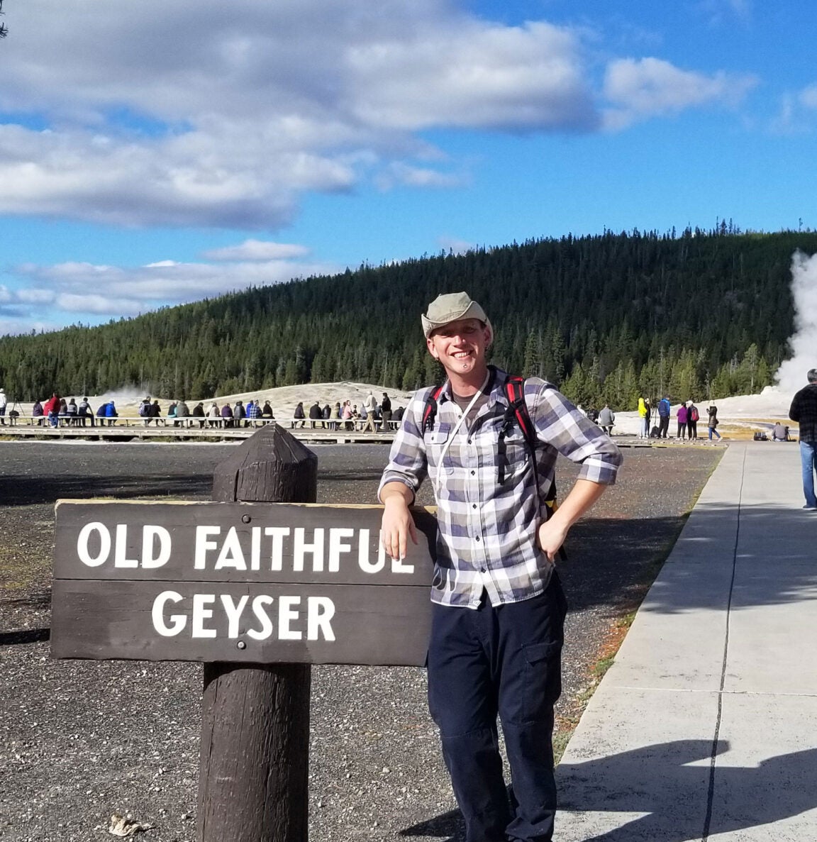 Jerry Mock posing by a board saying Old Faithful Geyser