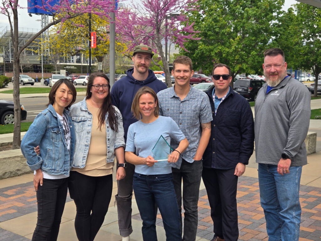 Dr. Brittany Brand holds an award, celebrating with her team members outdoors.