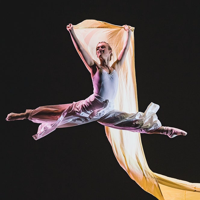A dancer jumps holding a flowing sash behind her