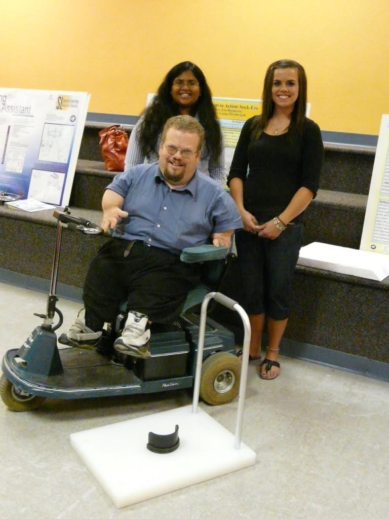 Three people, one using a mobility scooter, at a research presentation