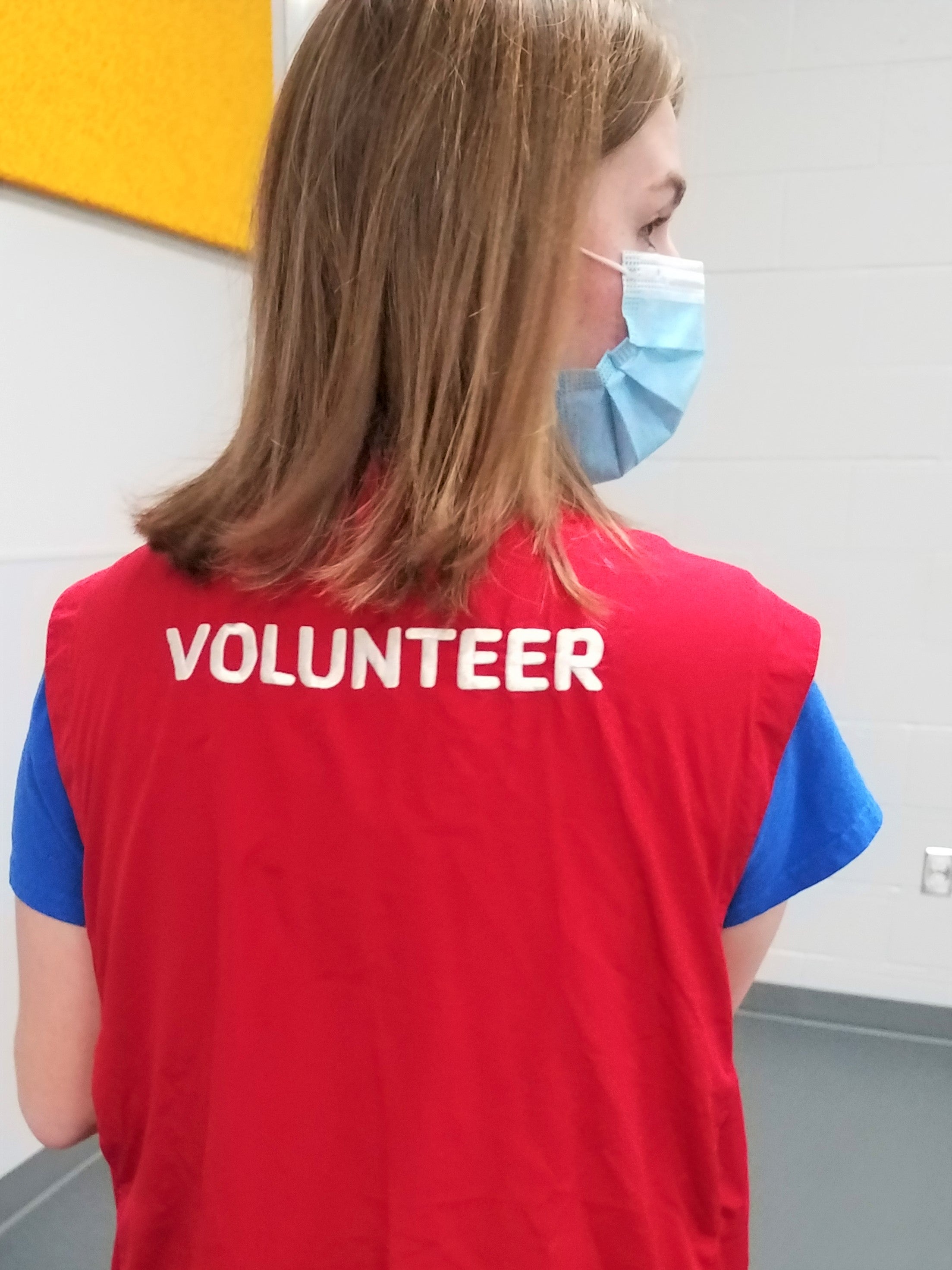 Person wearing a facemask and a vest with the word Volunteer stitched across the back
