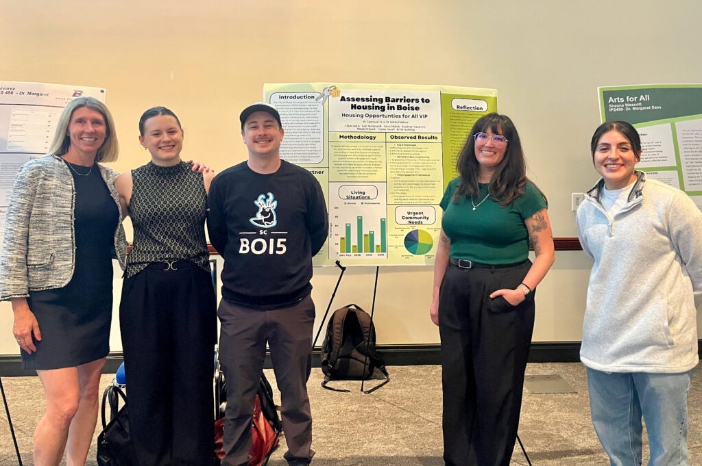 Five people stand in front of a research poster about barriers to housing in Boise.