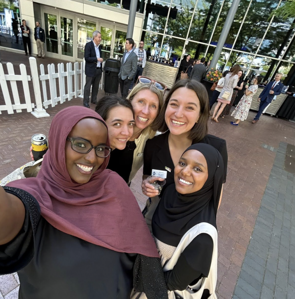 Five women stand together smiling.