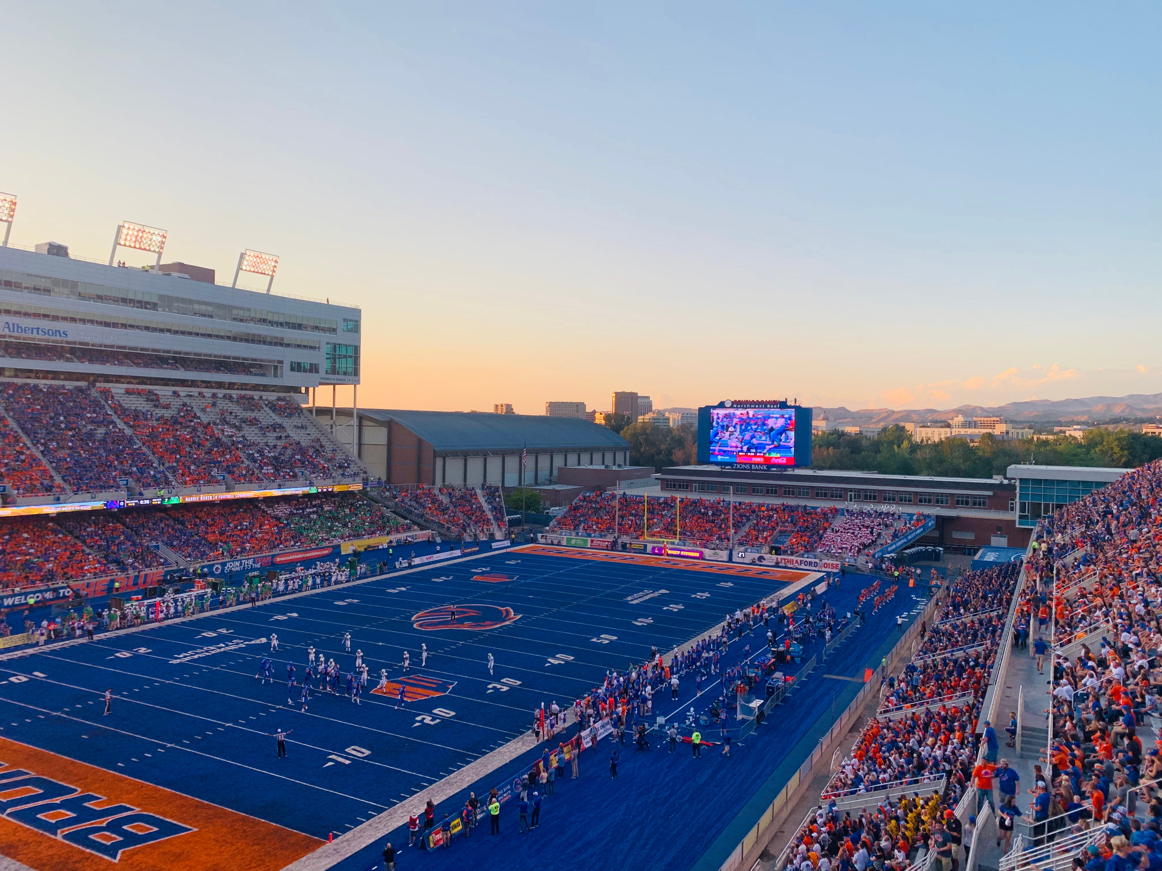 The Boise State Football stadium at sunset during game night with a crowd of people in the seats