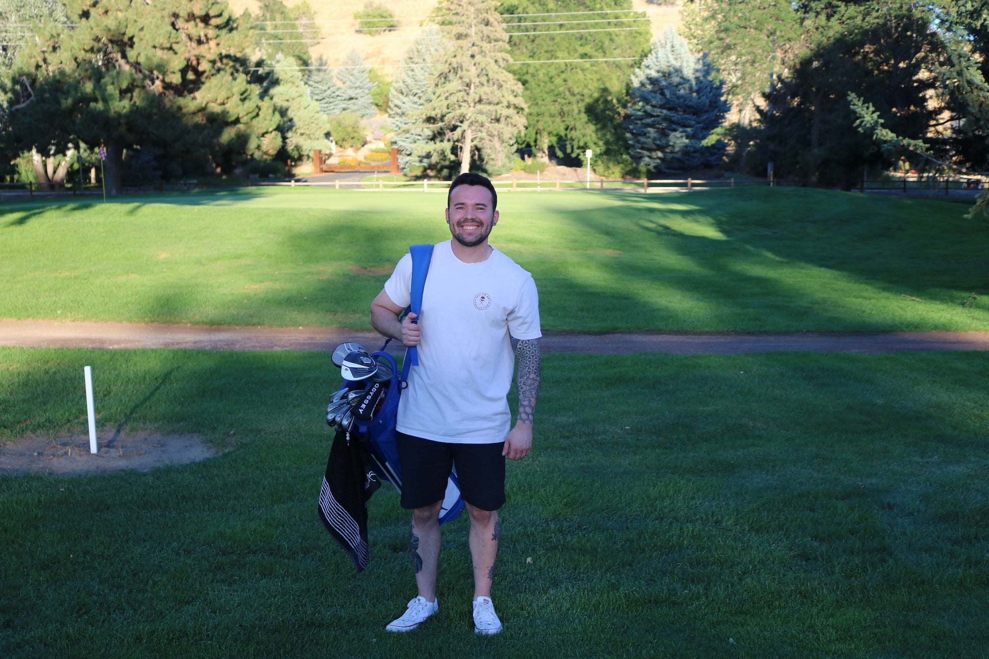 Chris Perry stands and smiles on the golf course with his clubs on his back